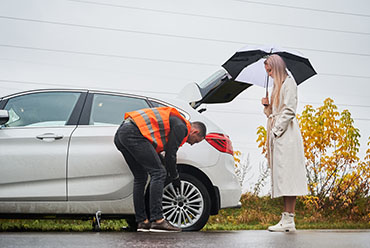 A man and woman stand beside a car, sharing an umbrella on a rainy day.