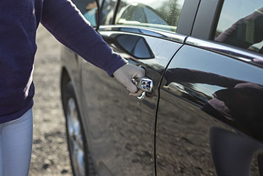 A woman is opening the door of a parked car, preparing to enter.