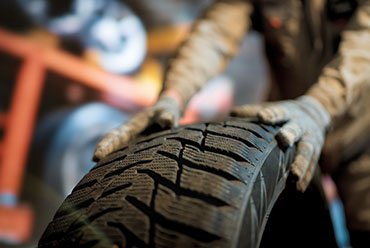 A man is holding a tire next to a car, preparing for a tire change or maintenance.